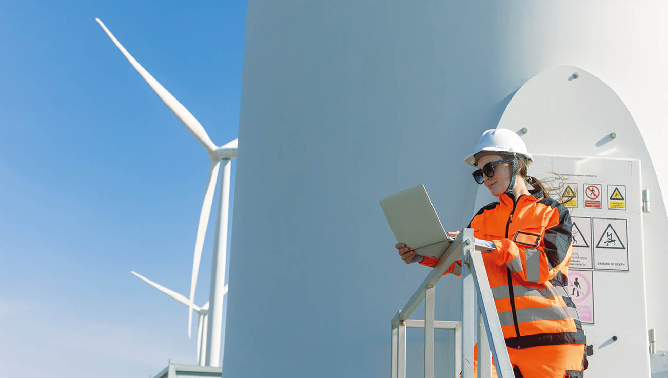 Frau in Arbeitskleidung vor einer Windkraftanlage