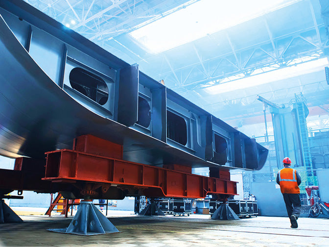 Arbeiter in einer Halle mit einem Teil eines Schiffsrumpfes