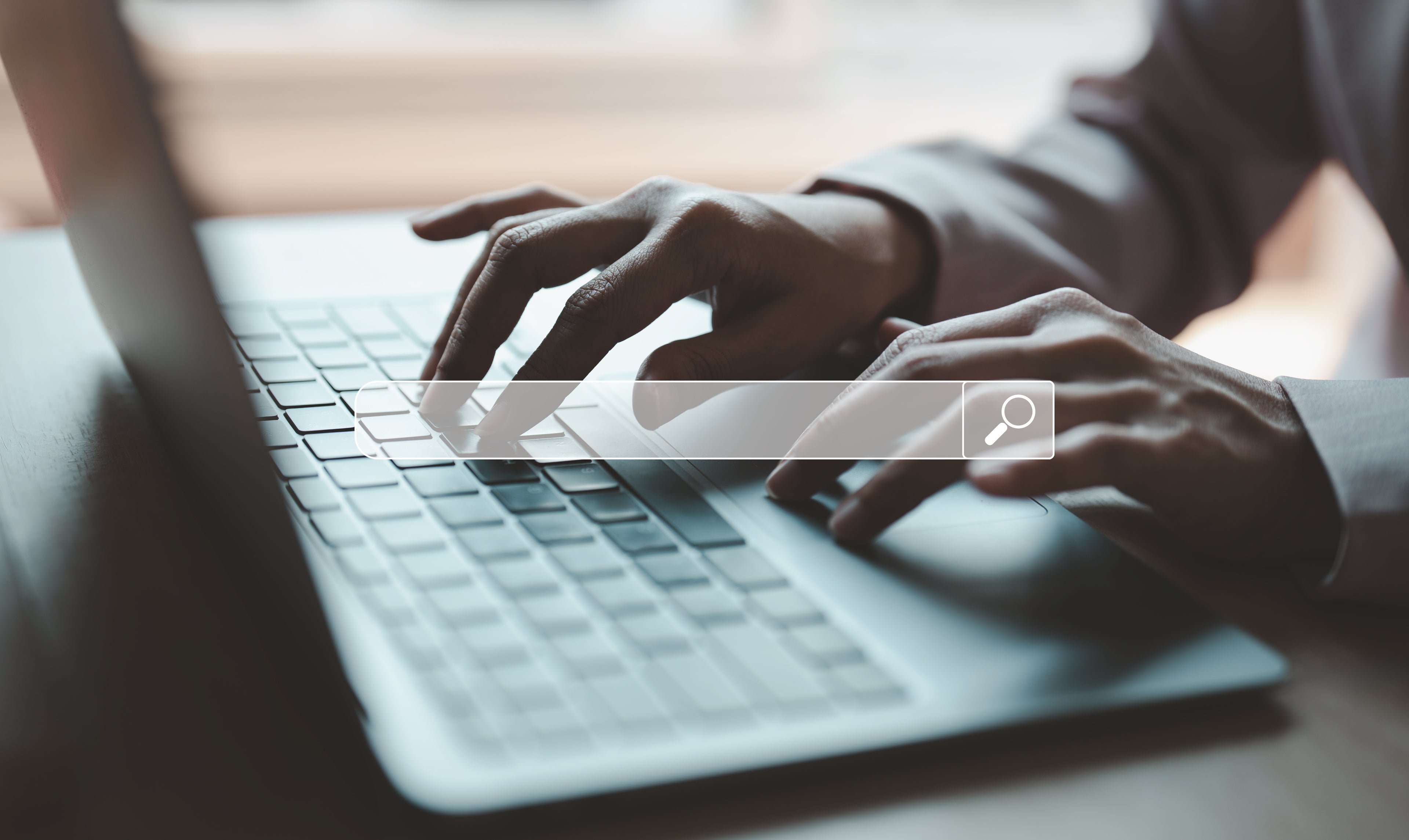 Hände tippen auf einer Laptop Tastatur mit Suchfeld im Vordergrund